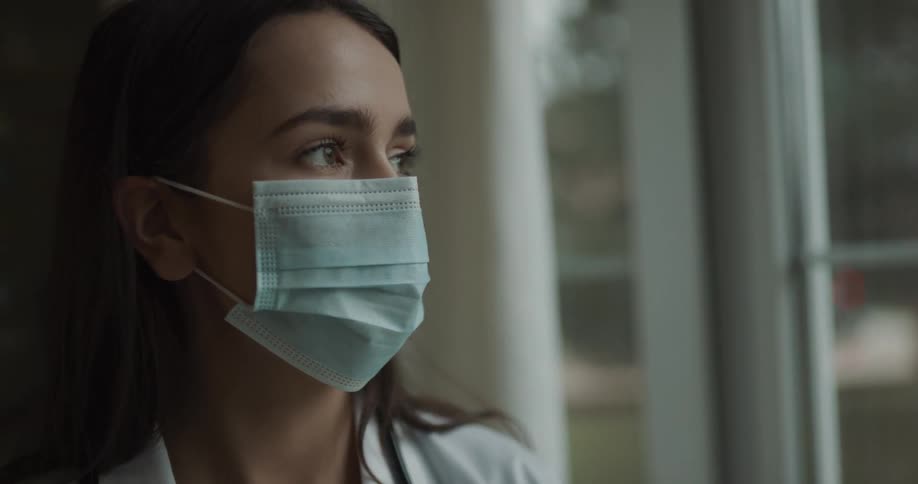 Doctor wearing a mask contemplating and looking through a window