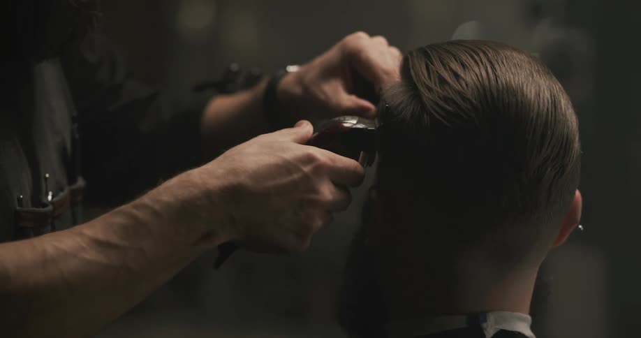 A barber combs a mans hair and then clips it