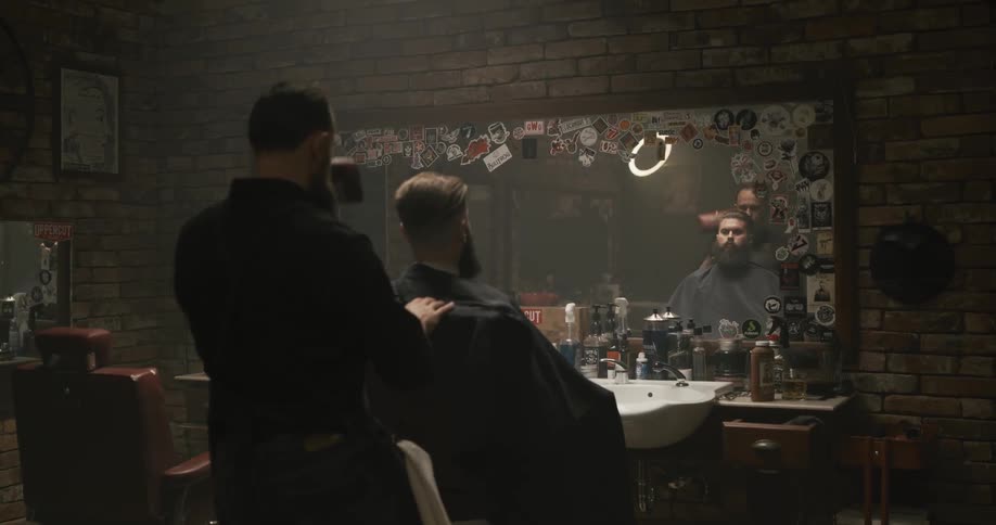 A barber raises the chair before reclining a customer with a full beard