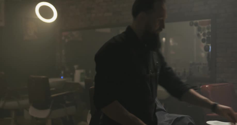 A stylist trimming the beard of a client in a barbershop