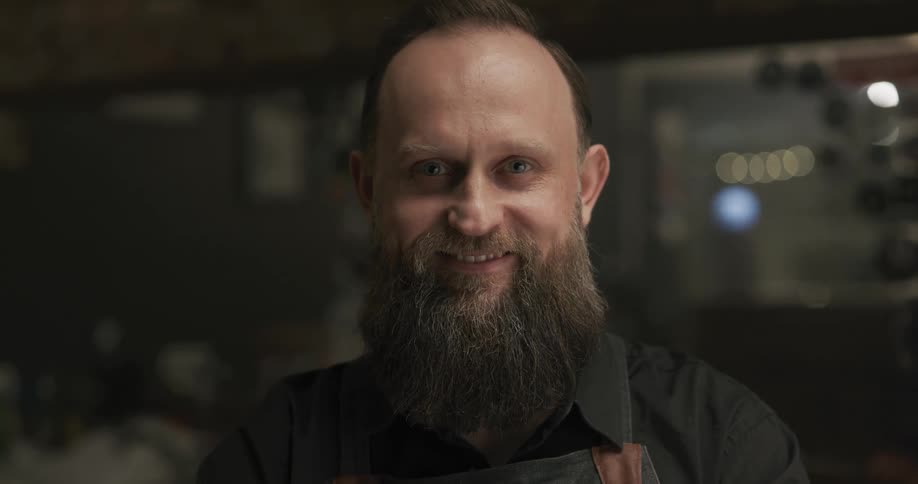 A man with a beard in a barbershop staring with a mirror in the background