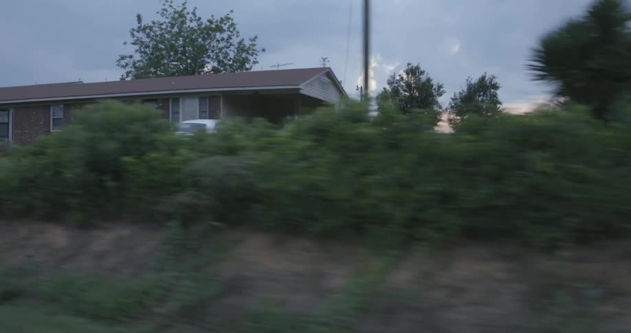 A house with grass and plants in the foreground with trees the sky and clouds in the background