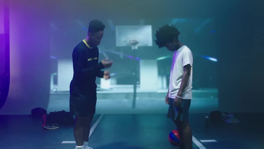 Two boys on a stage with one throwing a flat basketball on the floor