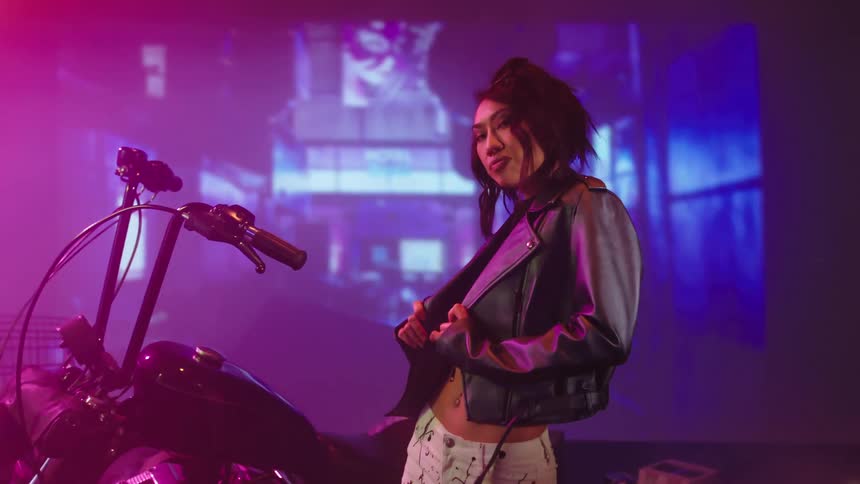 A model holds her leather jacket as she poses in front of a motorcycle and projected images