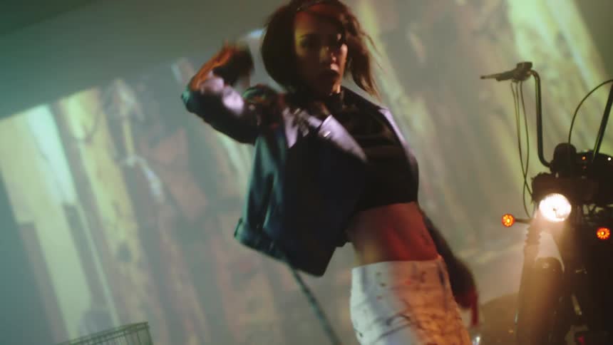 A woman on a stage dancing with a motorcycle and a shopping cart in the background