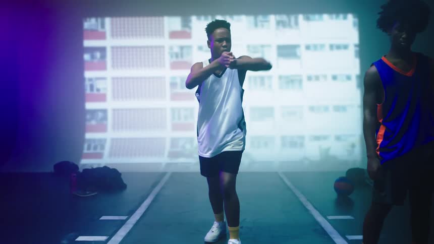 A teenage boys dances in front of a large screen playing a video as another teen stands by