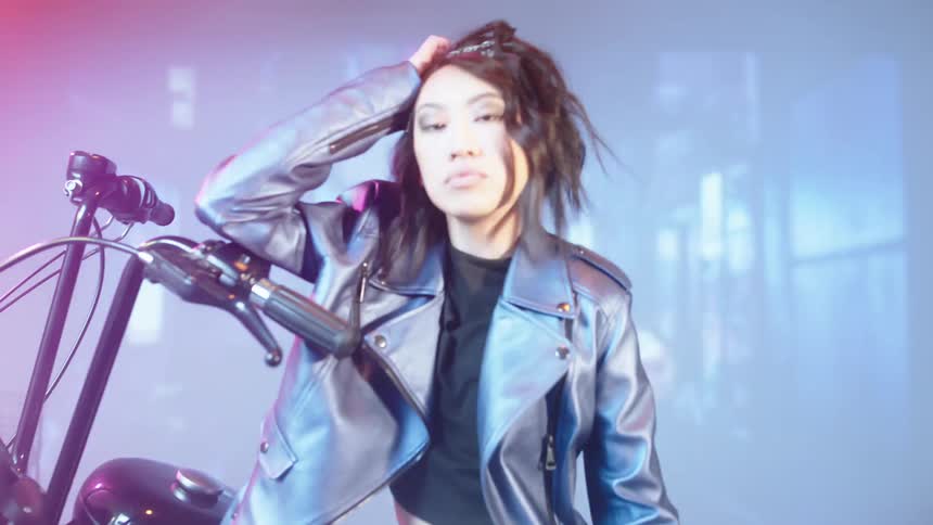 A model in a leather jacket poses against a motorcycle in a studio