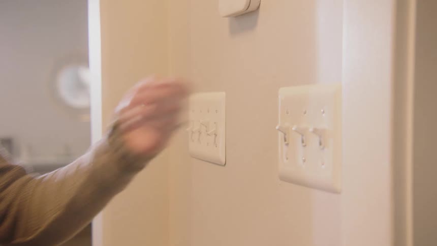 A woman flips light switches in the hallway