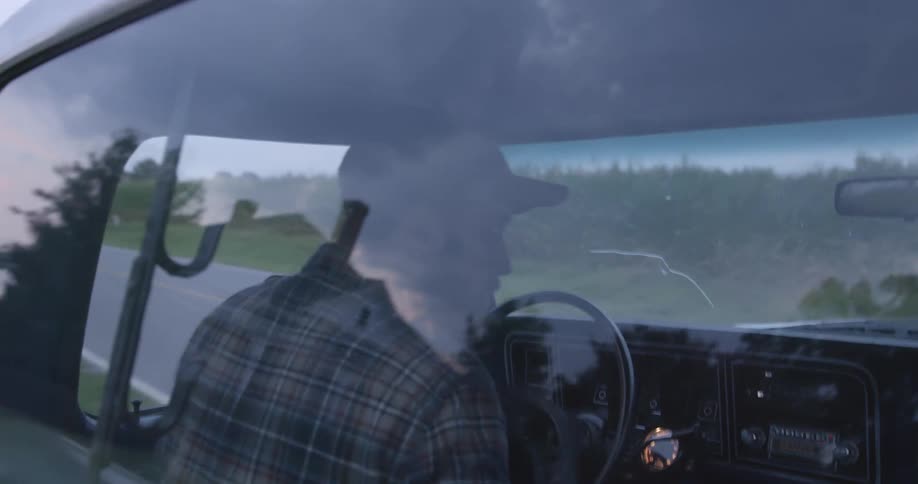 Man with cap beard and shirt drives car in the countryside