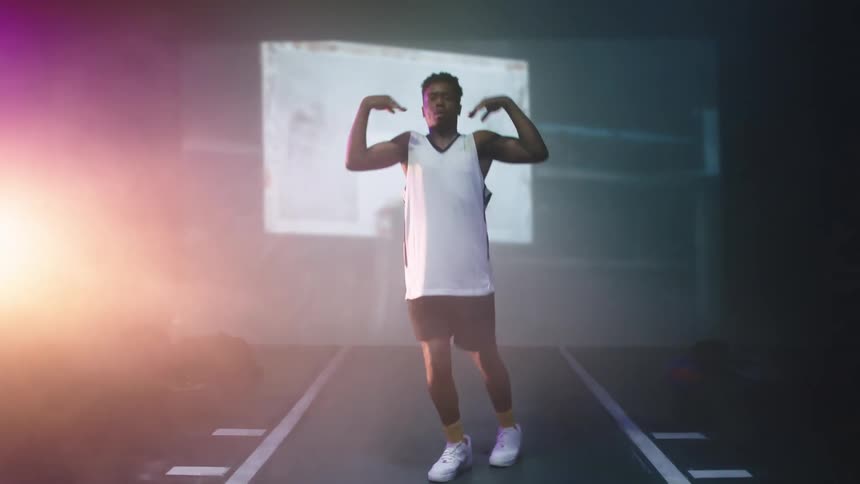 A man dances on a stage as scenes of a city flash on a projector screen behind him