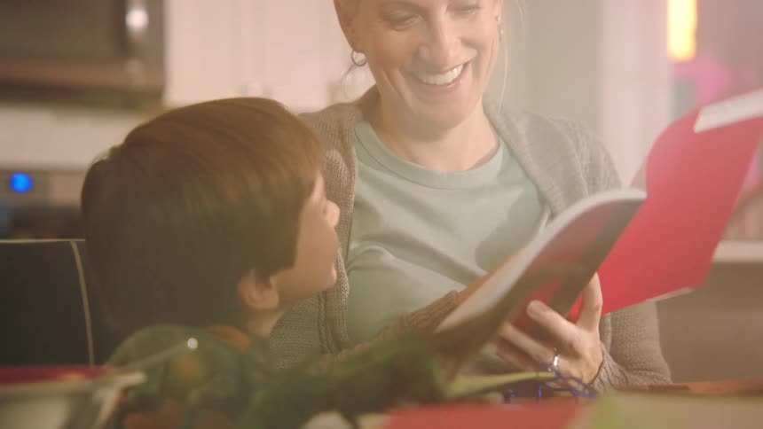 Grandmother and grandson smile while sitting reading in kitchen