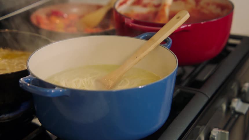 A person cooking several dishes over the stovetop in the kitchen at home
