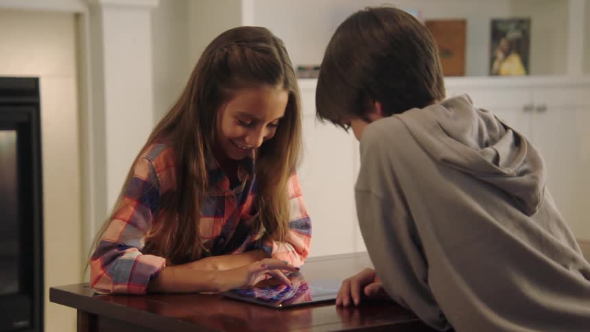 Two children take turns tapping and making a move while playing a game on a tablet