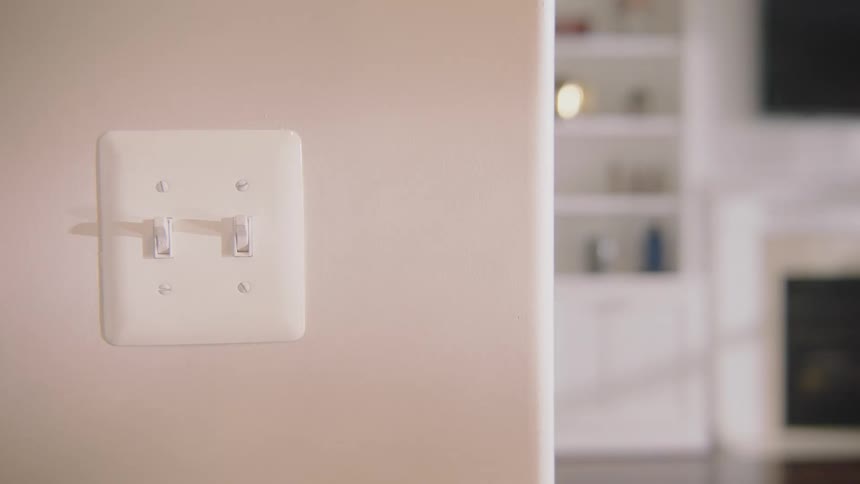 A young boy walks around a corner in his house and turns the light switches on