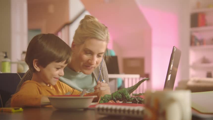 A woman and a boy in a room sitting at a table in front of a laptop