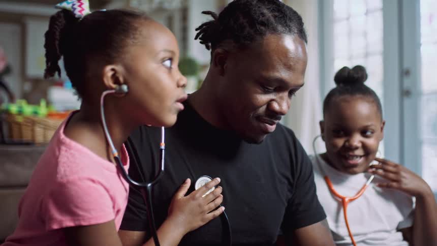 Two little girls at home with stethoscopes around their neck listen to their dads chest as he laughs