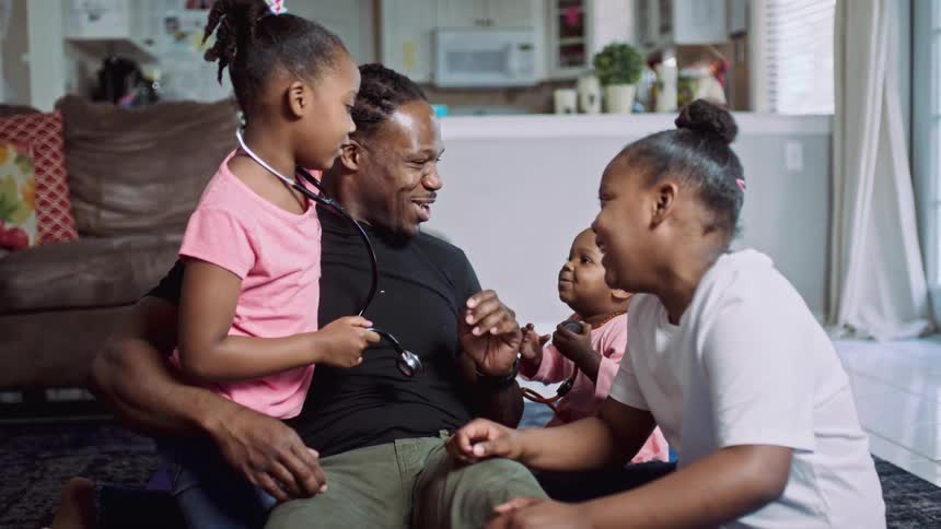 A father and daughters playing with a stethoscope and laughing