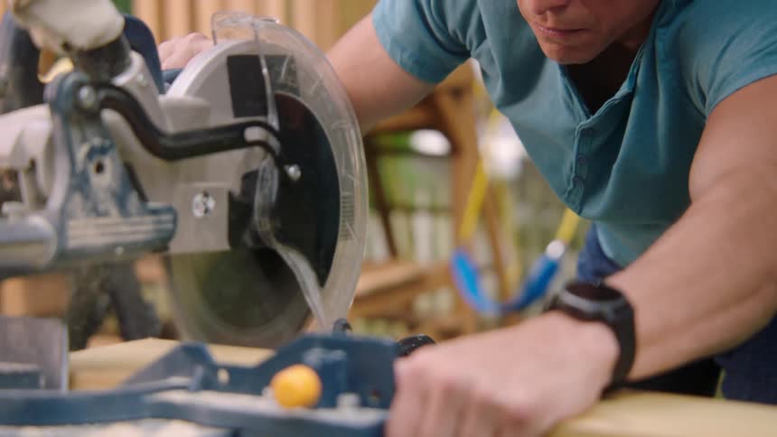 A man with goggles and a wristwatch using an electric saw to cut wood