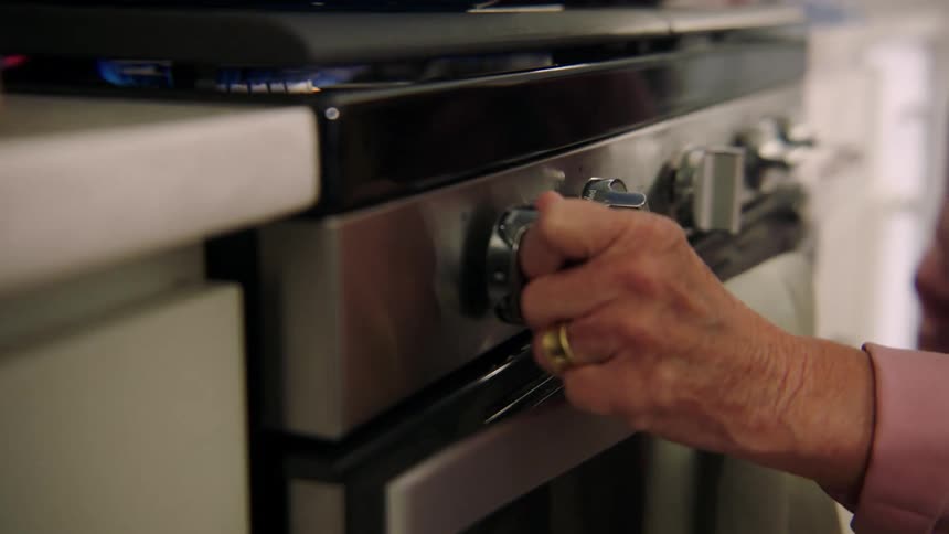 Older woman lowering heat on stove while cooking