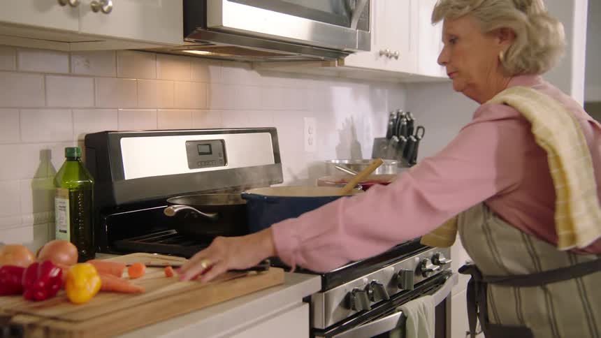 A woman in the kitchen with a apron stirring a pot on a stove