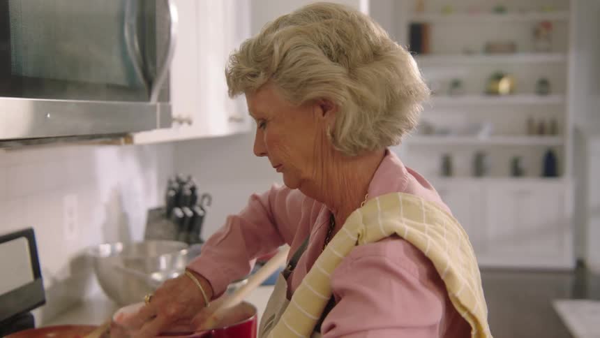 A woman with an apron in a kitchen stirring a pot on a stove