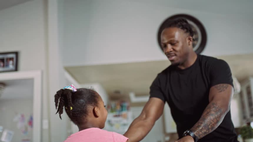 Father dancing with his daughter at the middle of the house next to the kitchen