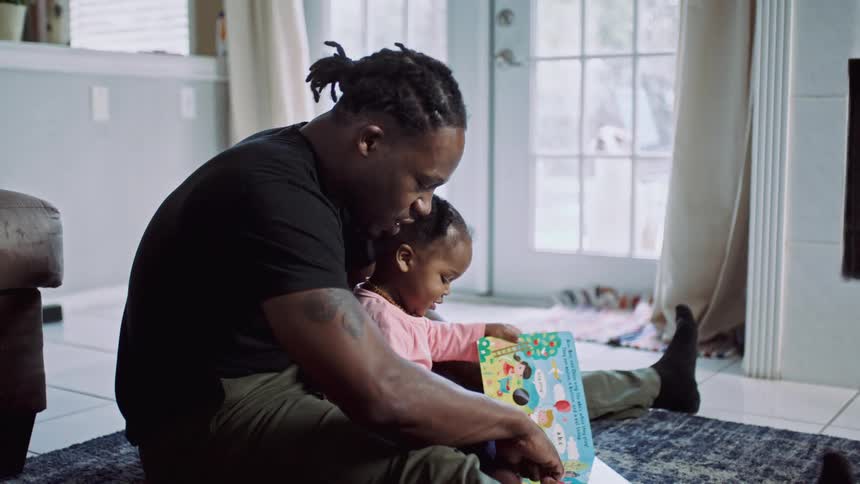 A man sitting on the floor with a girl reading a book with a door in the background