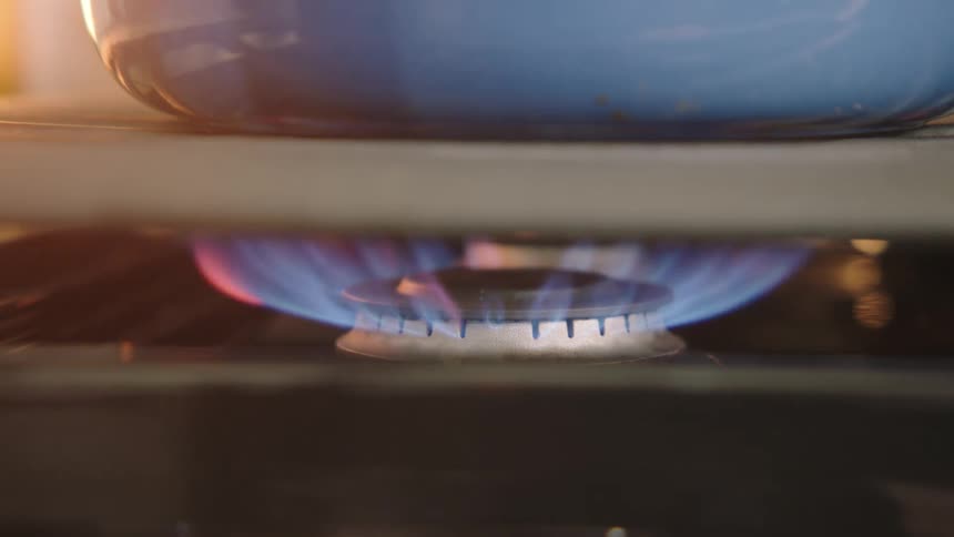 A burner lighting under a pan on a cooktop