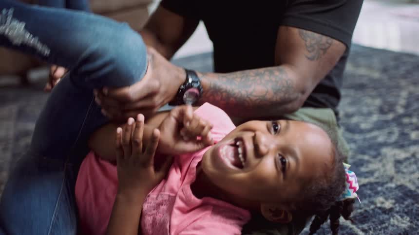 Father tickling and playing with his daughter sitting at rug on the floor
