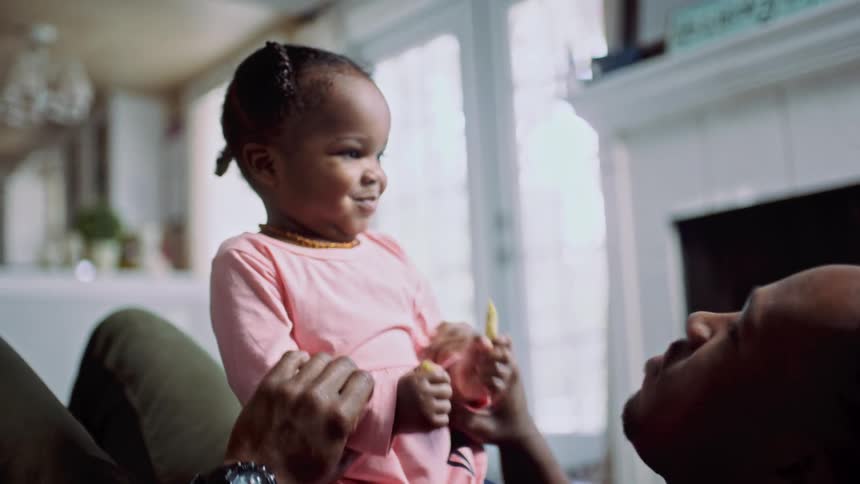A man in a room laying on the floor playing with a little girl with a fireplace and a door in the background