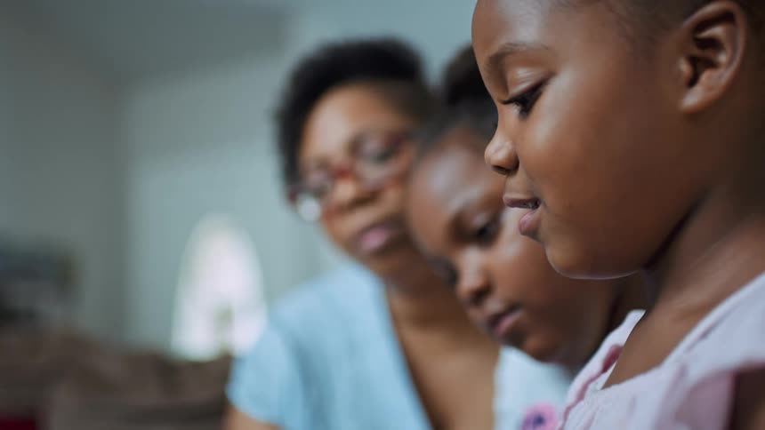 A woman reads aloud with her two young daughters at home