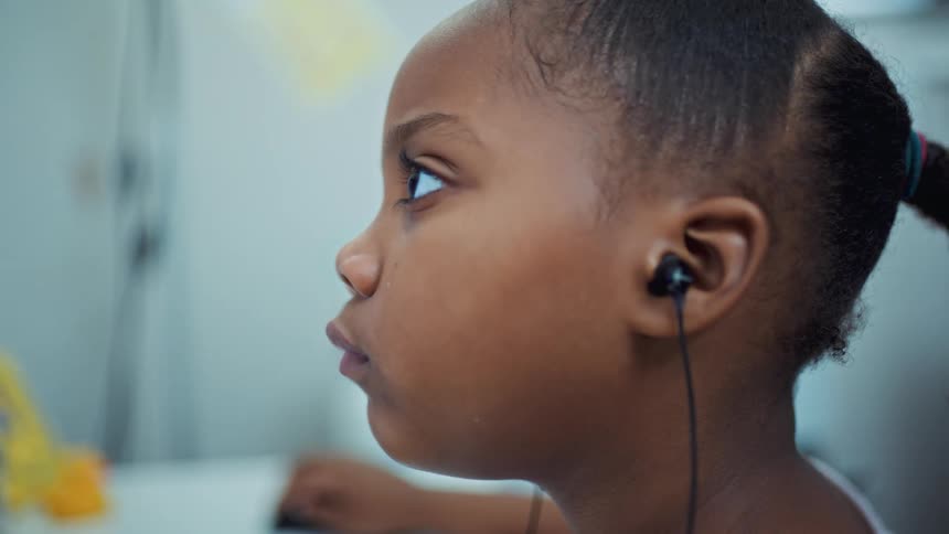 A young girl wearing earbuds uses a computer while sitting at a desk