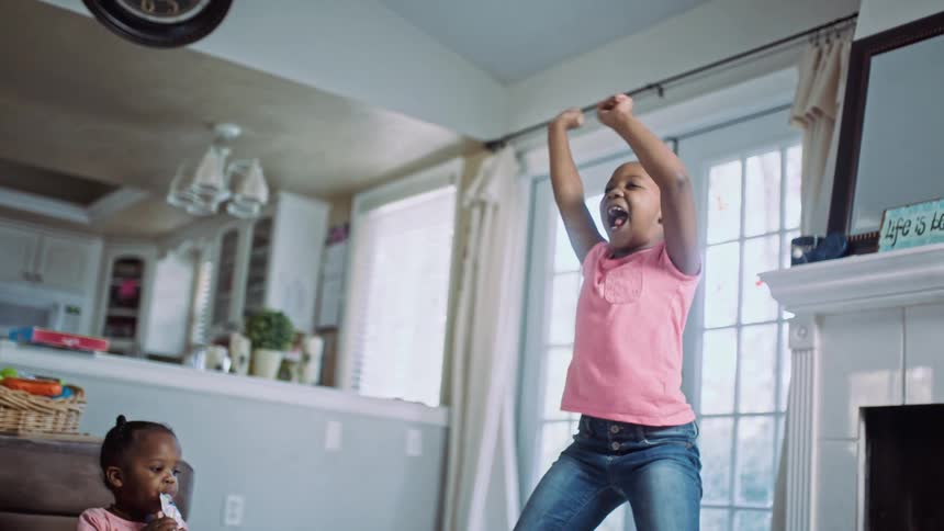 A little girl in a room jumping and dancing with a fireplace and doors in the background