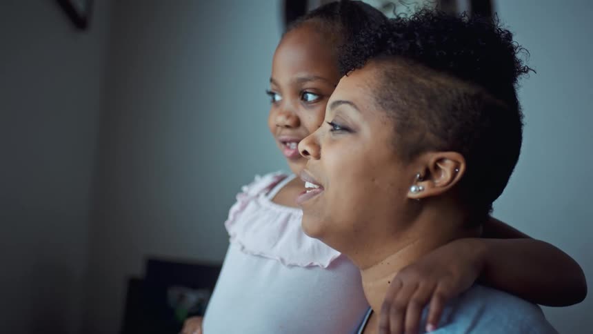 A woman and a little girl in a room hugging with a wall and a clock in the background