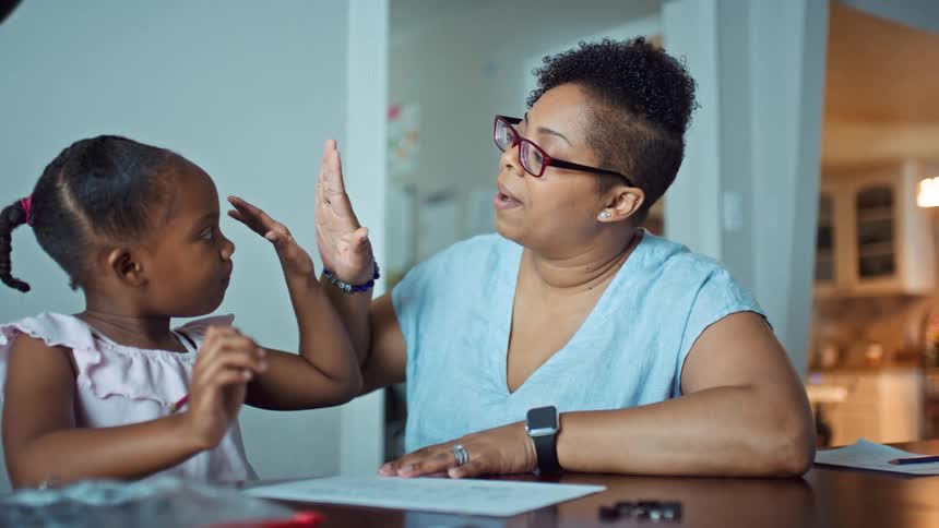 Mother and daughter sitting at the table at home while the mother helps her with homework