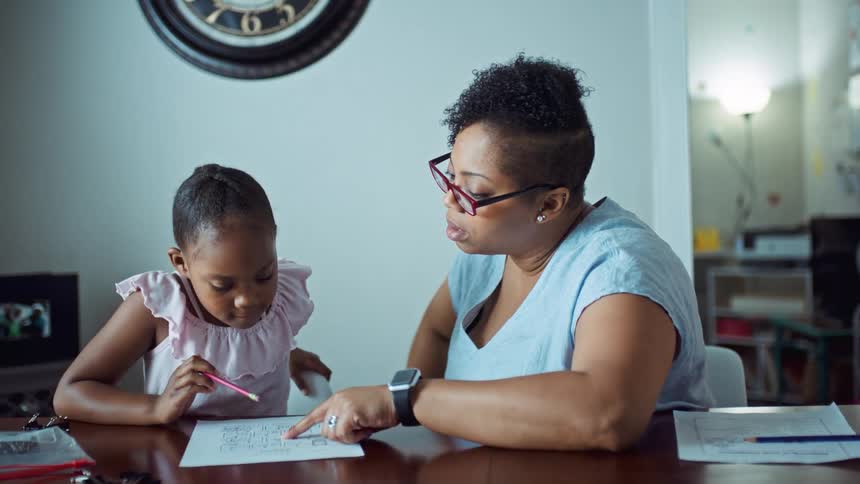 Mother teaching her daughter at home while sitting at the table