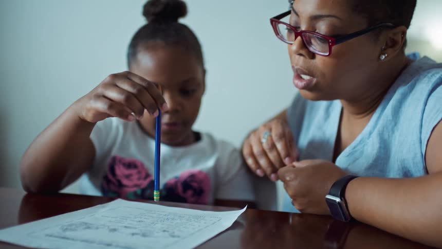 A woman and two girls sitting at a table looking at a paper with a wall in the background