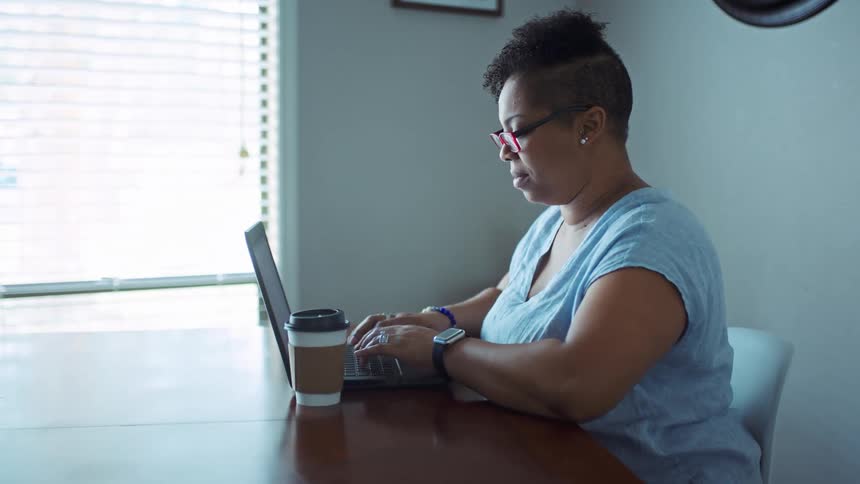 Black woman typing on her laptop while sitting alone at table