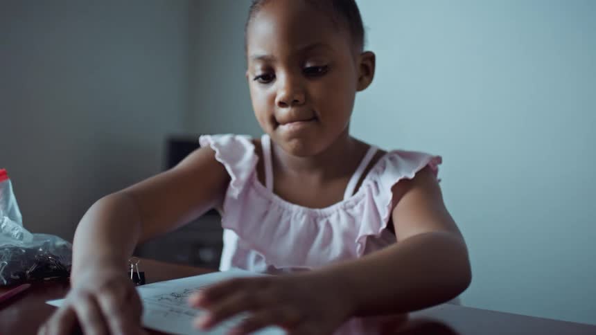 A young girl plays with paper clips at a table in a home