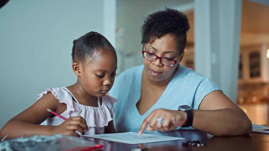 Mother and daughter sitting together at a table while the mother helps the daughter with homework
