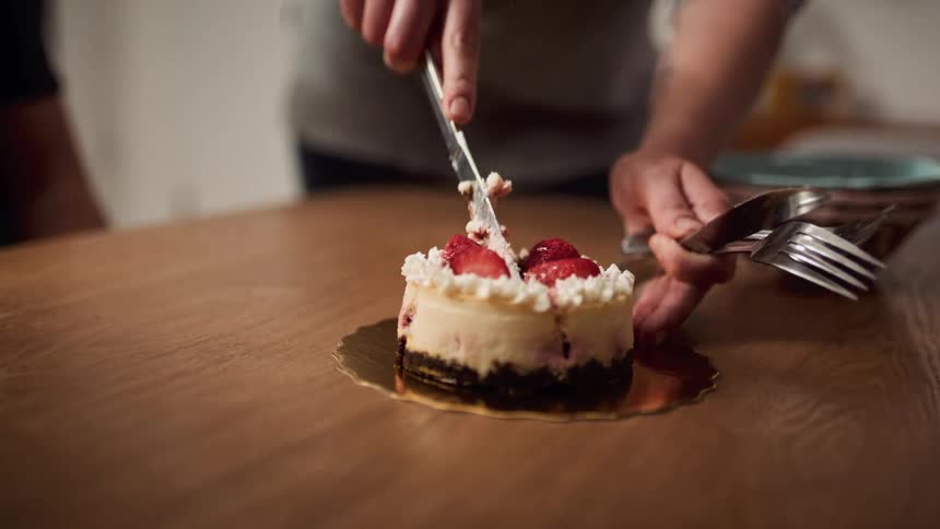A boy jumps up and down while waiting for his mom to cut a slice of cheesecake
