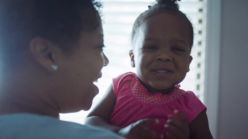 A woman laughs as the little girl she is holding makes faces