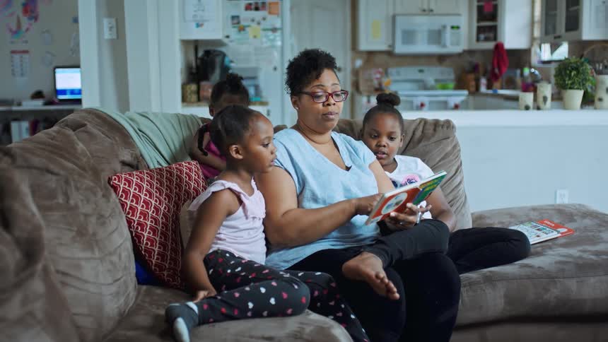A woman and tree girls sitting on a couch reading a book