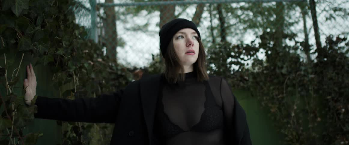 White young woman wearing a overcoat and beanie leaning over a wall for a photo shoot