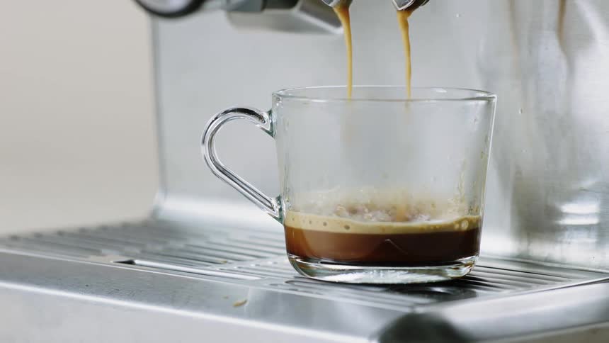 Espresso drips from two spouts on an espresso machine into a glass mug