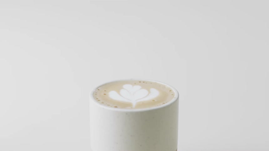 A coffee in a cup with a design on the foam with a white background