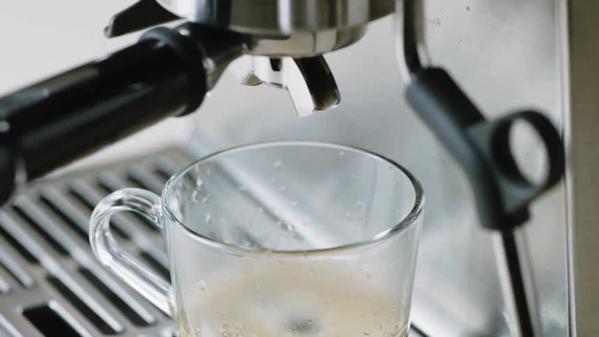 Coffee drips from the nozzle of a coffee machine into a glass coffee mug