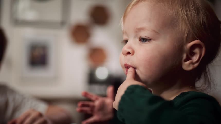 Baby sitting at the table and eating food with his hands