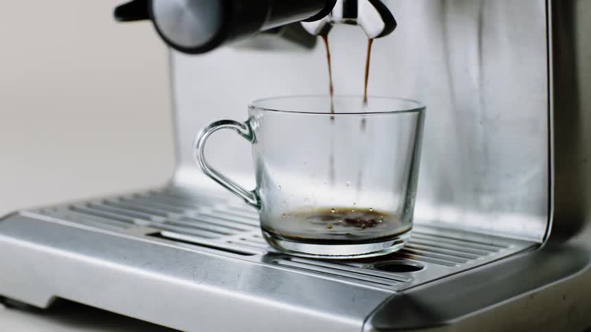 A coffee machine slowly drips coffee into a glass coffee mug