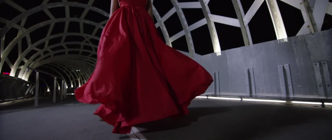 A woman in a long red gown runs and twirls around in a tunnel